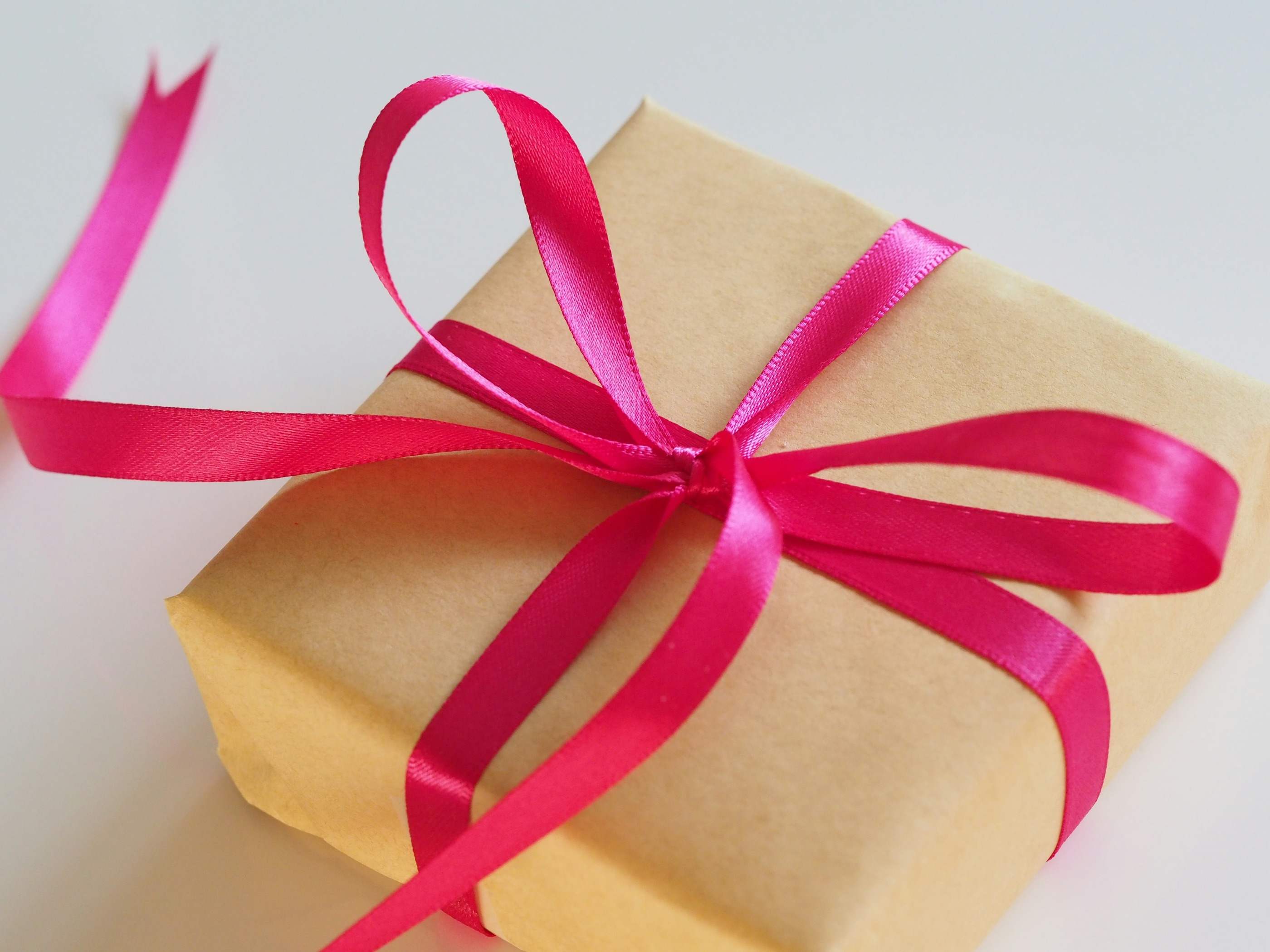A gift box wrapped in kraft paper and tied with a bright pink satin bow