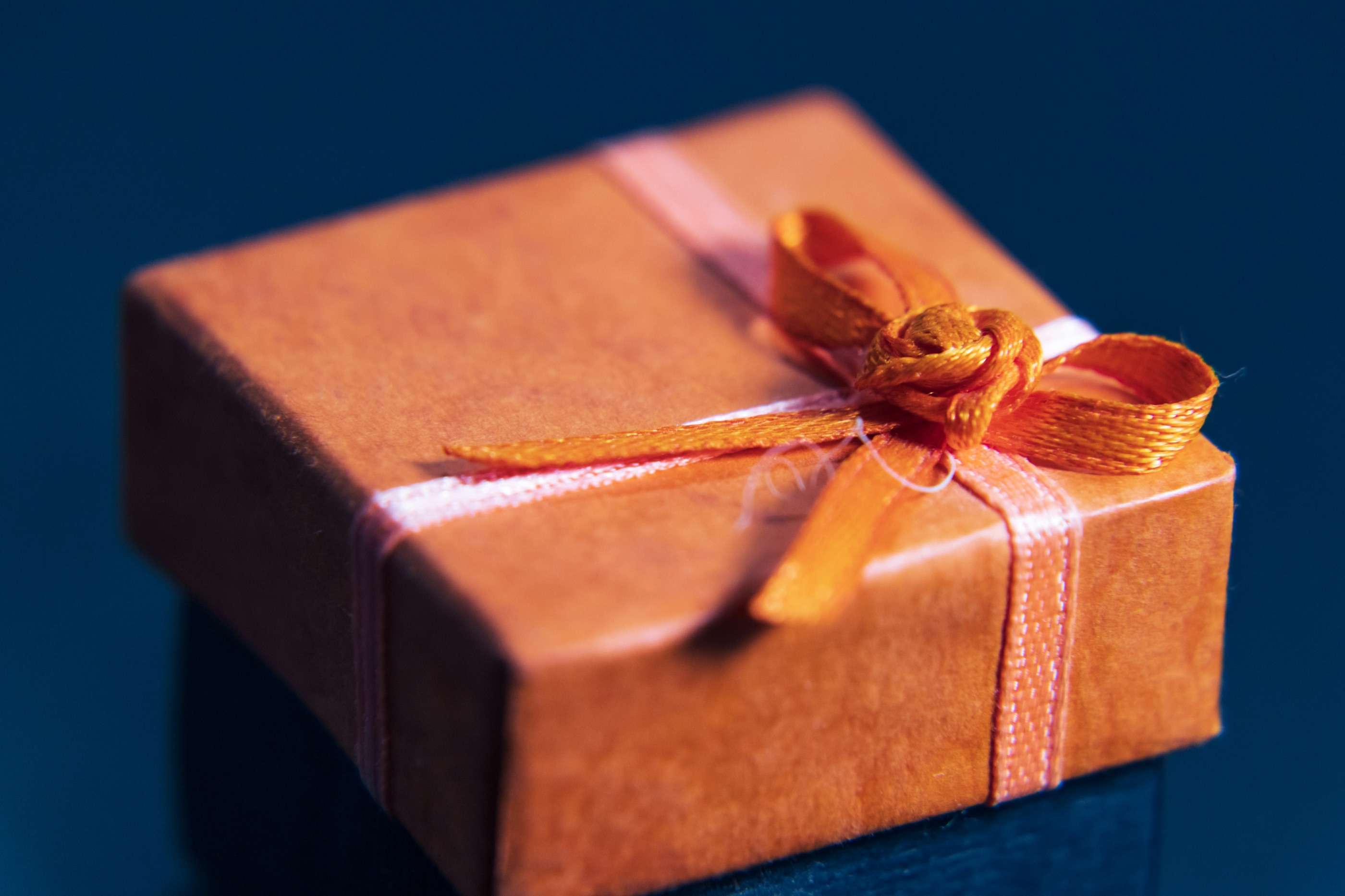 A small copper-coloured gift box tied with an orange ribbon, against a deep navy background