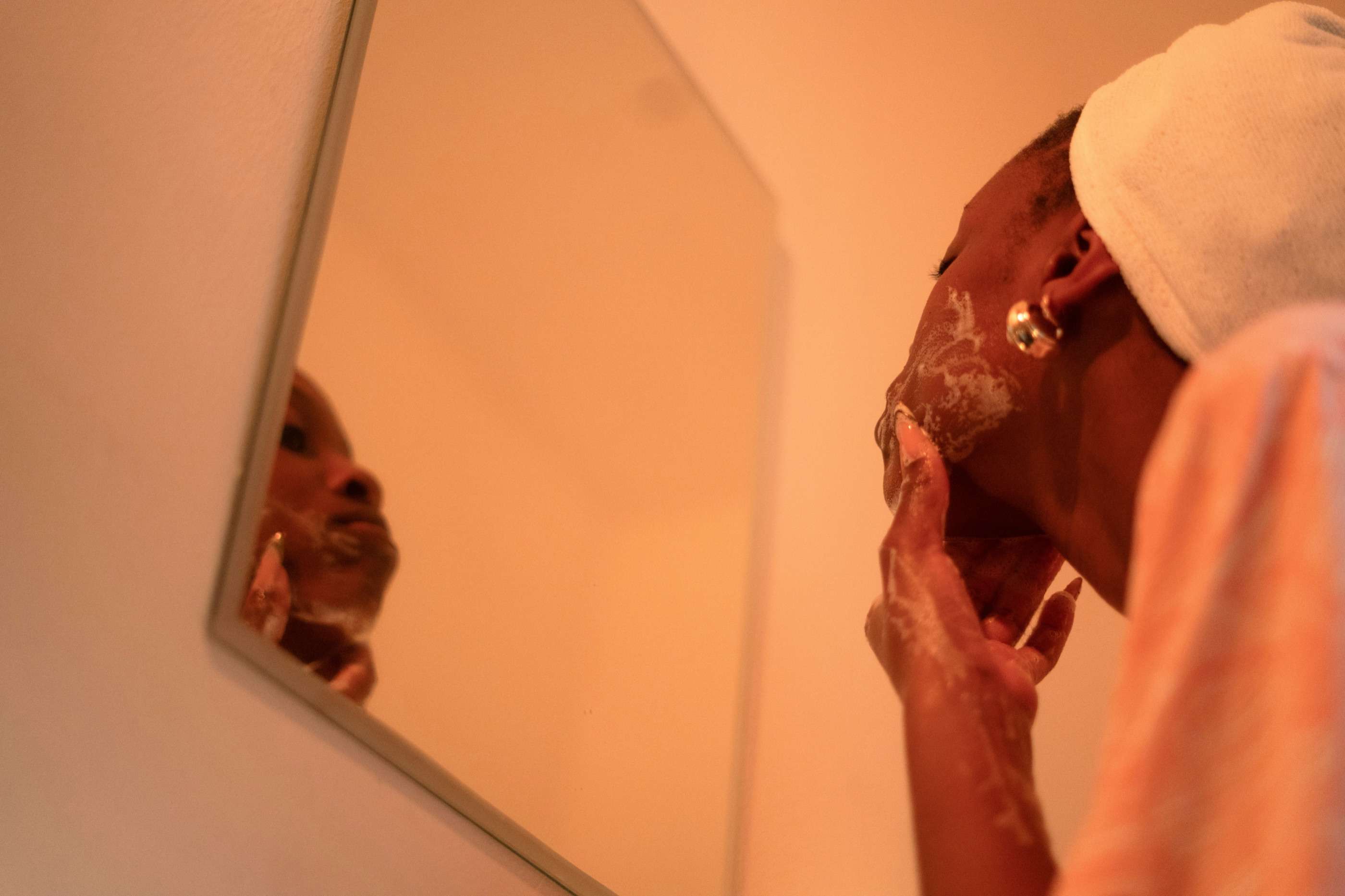 A man spreading shaving foam along his jaw while looking into a mirror, in warm orange light